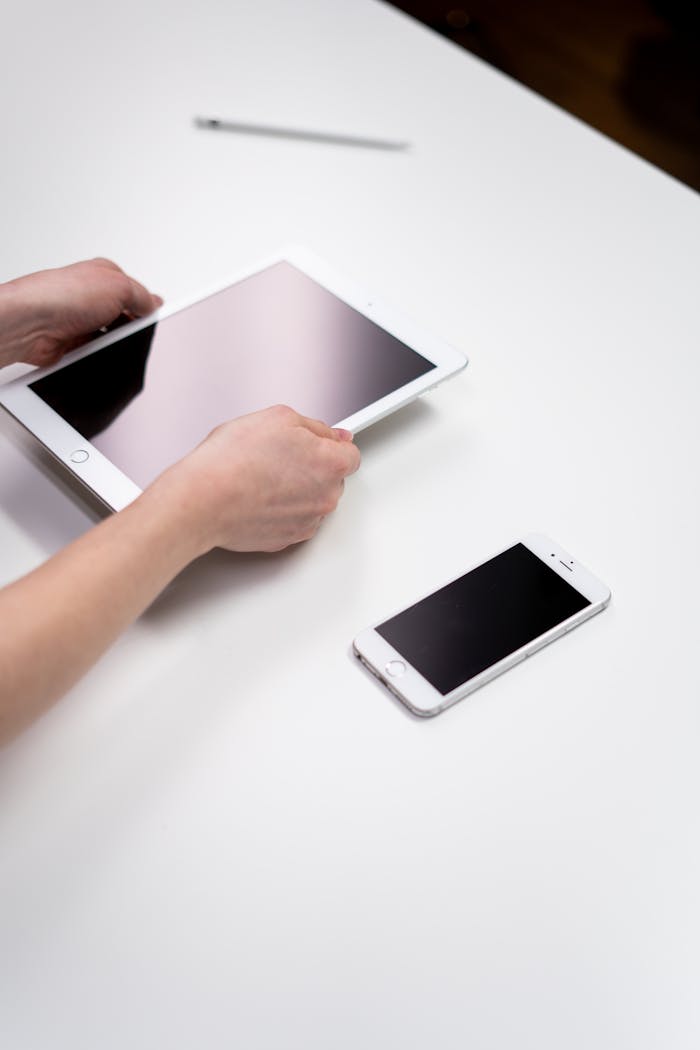 Hands interacting with a tablet and smartphone on a white table, showcasing modern technology.